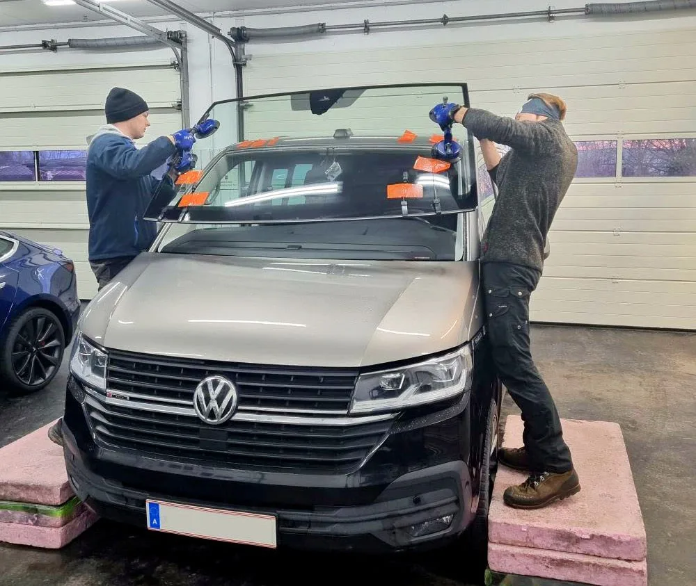 Zwei Mitarbeiter tauschen die Scheibe eines VW-Busses