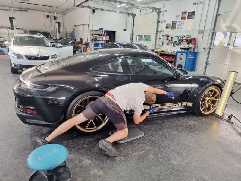 Mitarbeiter arbeitet mit einer Dellenlampe an einem Porsche