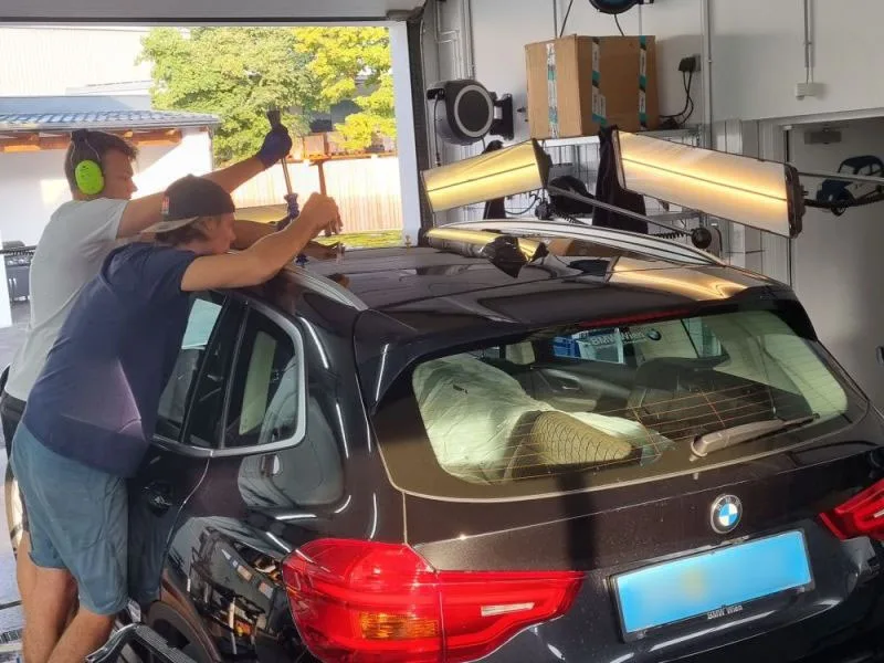 Zwei Dellentechniker arbeiten mit Lampen an einem Fahrzeugdach